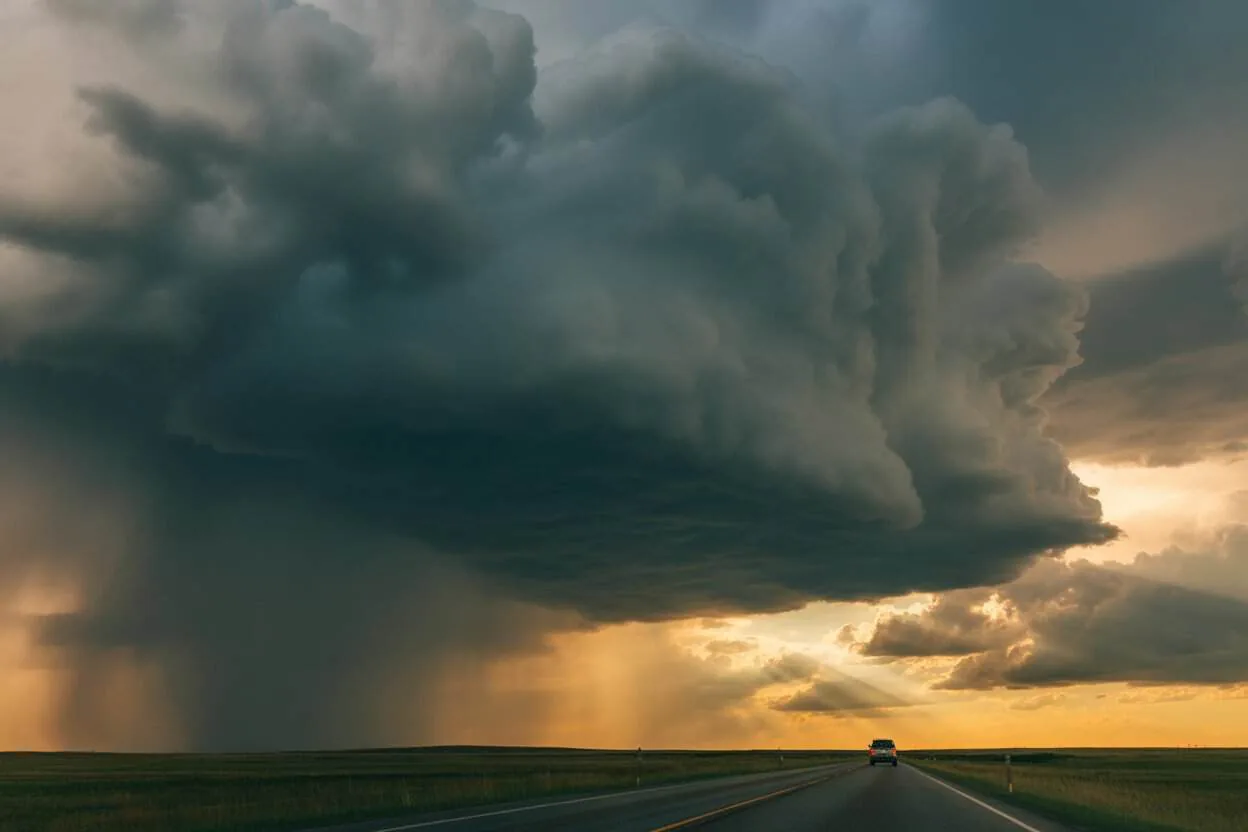 Dark storm clouds building over open Plains highway with a travel vehicle in the distance